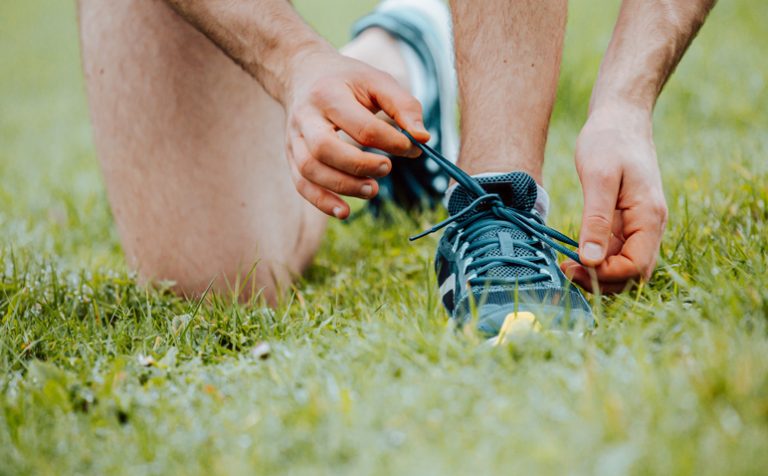 A super close up of a man tying the shoelaces on this sport shoes over green grass before training fitness