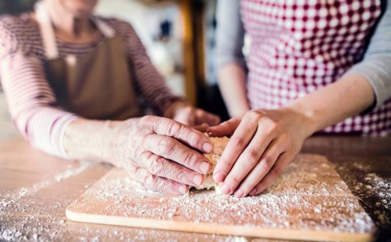 An unrecognizable elderly grandmother with an adult granddaughter at home, baking.