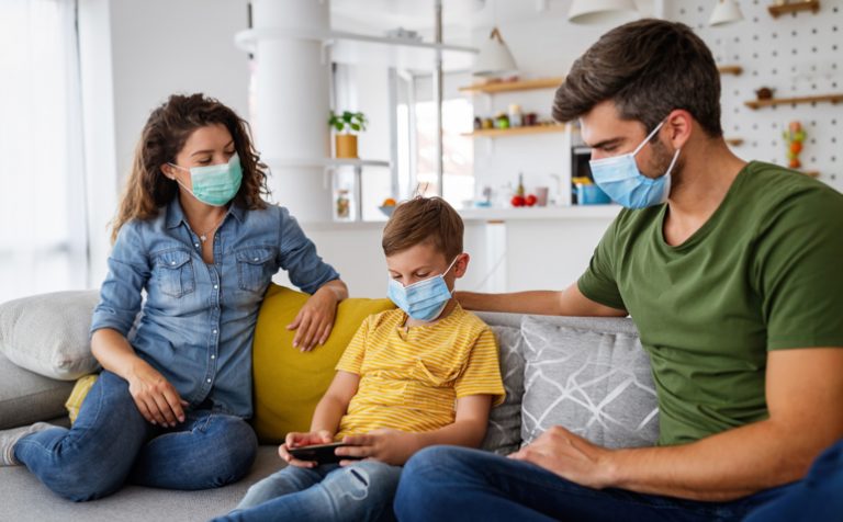 Beautiful young family wearing face masks against coronavirus world pandemic and staying home