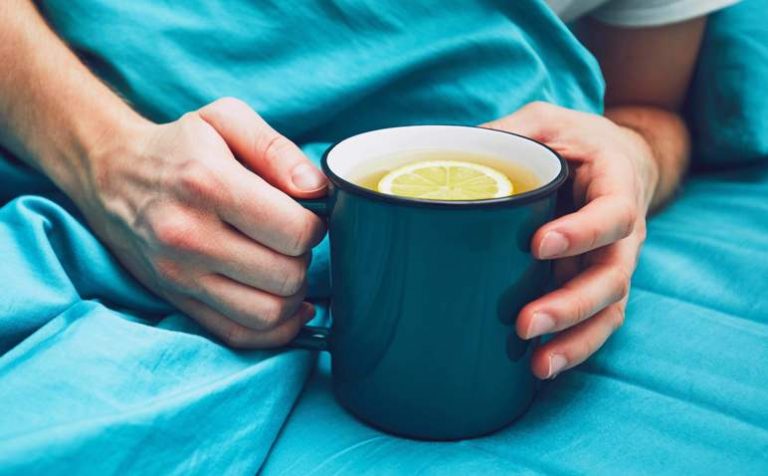 Influenza season. Hand of the sick man holding cup of the hot tea in the bed.