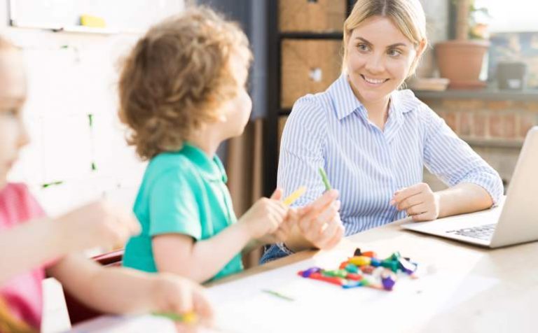 Happy mother playing with her two kids while working on laptop