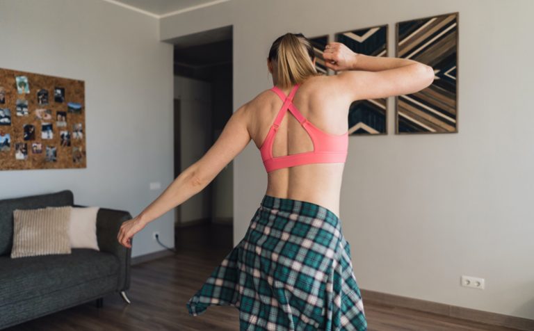 Active young woman in sportswear clothes dancing in living room with cozy, modern interior, enjoy life concept. Occupation during isolation at home.
