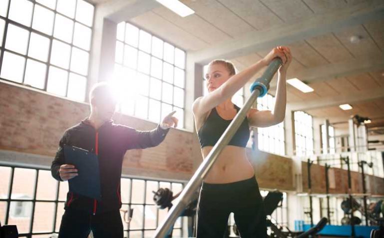 Fitness woman exercising with fitness trainer in gym. Female working out with her personal trainer at health club.